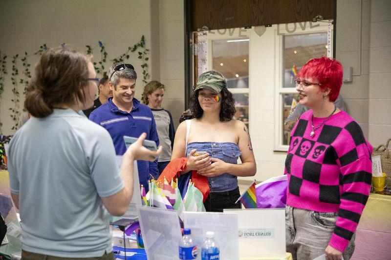 Two students and a faculty member stand at a table with pride flags.