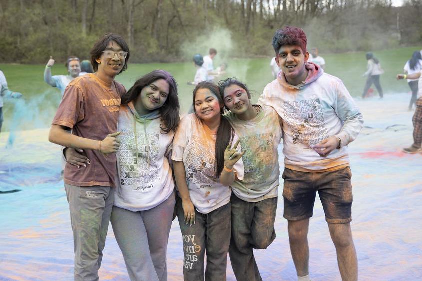 Five students covered in colorful dust smile for the camera.